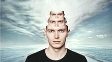 man with two copies of his face nesting on top of his head, with ocean and sky behind him